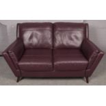 A plum leather two seat sofa raised on small wooden feet.