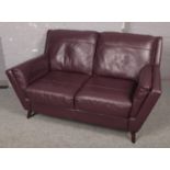 A plum leather two seat sofa raised on small wooden feet.