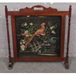 A mahogany framed painted fabric fire screen, depicting a peacock.