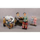 A group of Laurel & Hardy ceramic figures, sat on bench, with jail clothing on, on suitcase trolley,