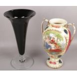 A large black glass art vase along with a ceramic twin handled vase depicting figures.