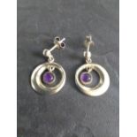 A pair of white metal annular drop earrings, with amethyst cabochon inner drop