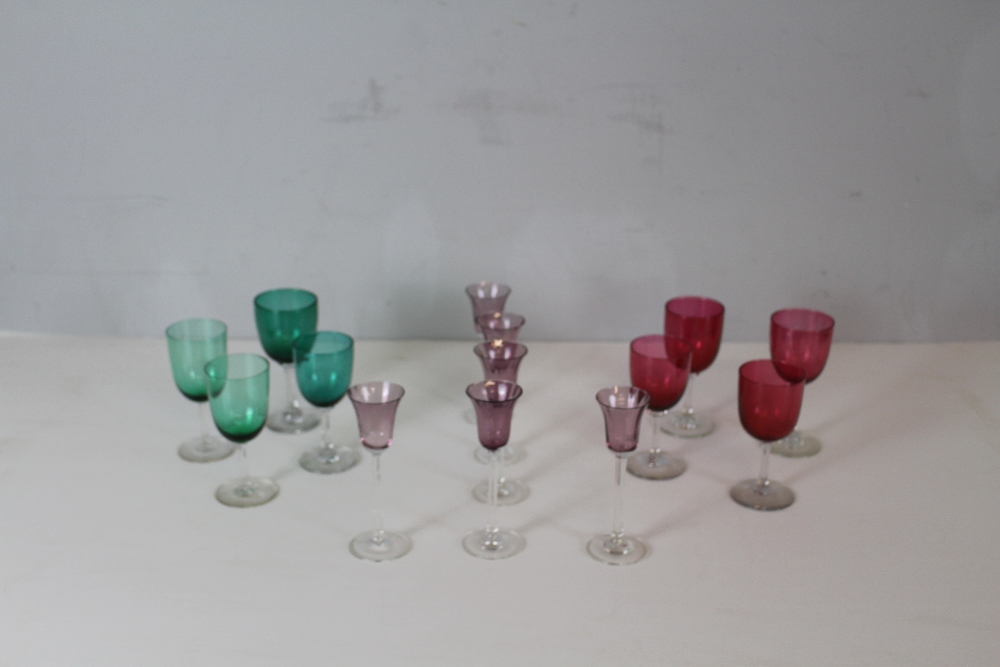 A selection of coloured wine glasses, four cranberry tined, four green tinted and six amethyst