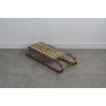 A vintage red-painted tubular steel sledge with slatted seat 80cm