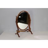 A George III style mahogany oval skeleton toilet mirror, the bevelled mirror plate between slender