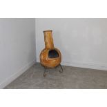 A moulded terracotta garden chiminea, with metal stand and green canvas protective cover 95cm x 45cm