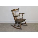 A stained wood rocking chair in the style or Ercol, with spindle supports and shaped arms 84cm high