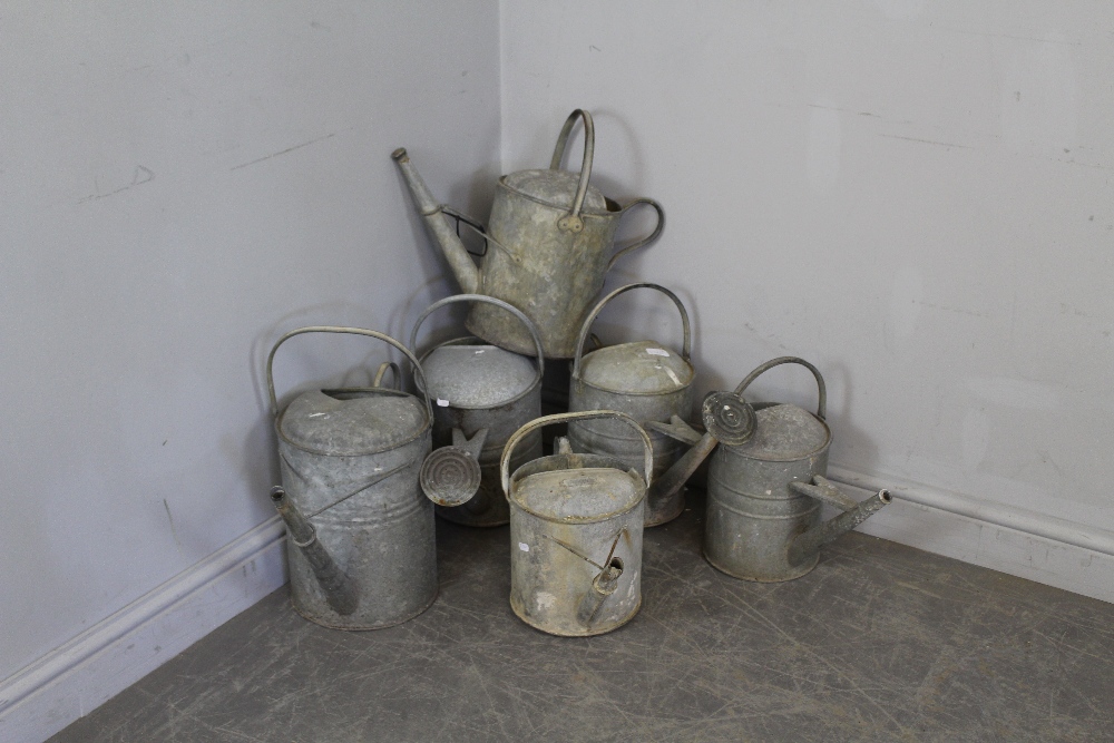 A group of six vintage galvanized watering cans, each with rear and over handles, two complete