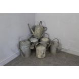 A group of six vintage galvanized watering cans, each with rear and over handles, two complete