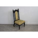 A Victorian ebonised low chair, having a padded arched back between ring-turned supports, the padded