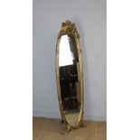 A reproduction oval gilt dressing mirror, of oval form with scrolled foliate crest and reeded