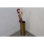 An embossed brass cylindrical stickstand 52cm high with two walking sticks and two umbrellas, good