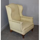 An Edwardian upholstered wing-back armchair, with patterned cream upholstery and short cabriole