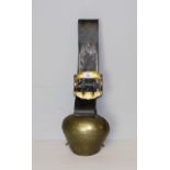 A large vintage brass cow bell with simplistic waved line decoration and broad leather strap with