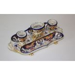 An early 19th century Derby porcelain inkstand, having three central urn-form wells flanked by