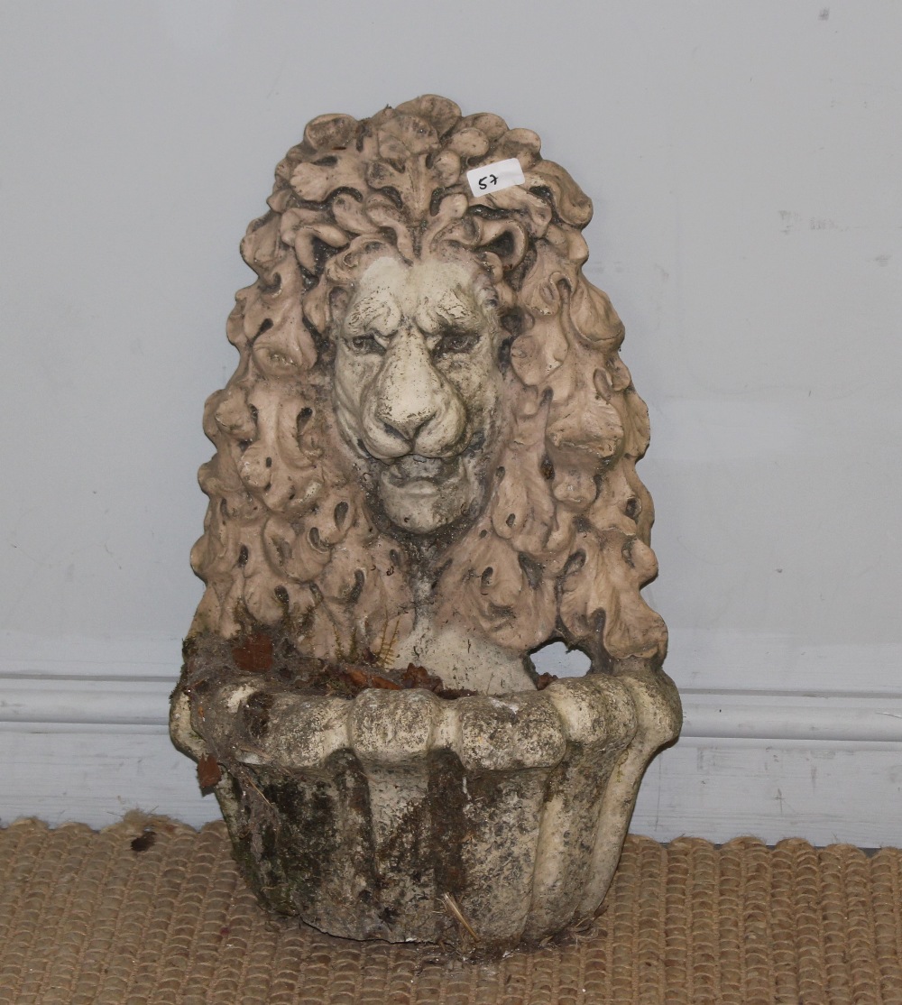 A cast composite stone wall font, with lion mask within an oak leaf surround, over the fluted well