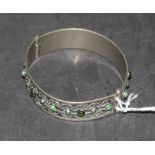 A white metal bangle, decorated with repeating pattern of applied wire and small green stone