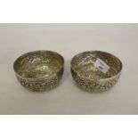 A pair of Indian white metal finger bowls, embossed with bands of foliate scrolls