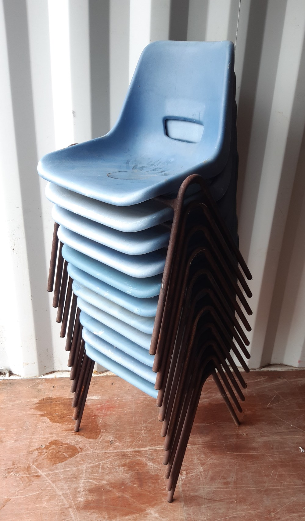 A set of 11 blue plastic stacking chairs, rusted and with one seat damaged