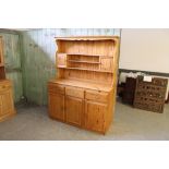 A modern pine kitchen dresser, the upper stage with shelves and small cupboards. The base with three