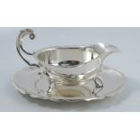 A silver sauce boat and stand, with shaped edge and open scroll handle, the stand with shaped