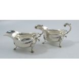 A pair of silver sauce boats, with shaped edge, leaf scroll handle and raised on three legs with pad