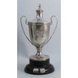 A covered silver trophy cup, engraved with a presentation inscription, raised on a pedestal with