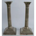 A pair of silver Corinthian column candlesticks, with fluted columns, raised on a stepped square