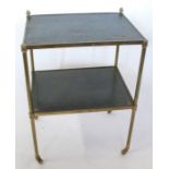 A brass set of shelves, the two shelves with tooled leather tops, on casters, 18.5ins x 14ins x