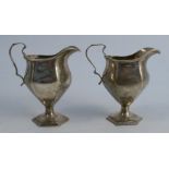 A pair of silver jugs, with faceted bodies, raised on a pedestal foot, Birmingham 1911 and 1914,