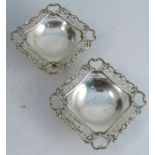 A pair of silver dishes, of square form with pierced edges, raised on a pedestal with square base