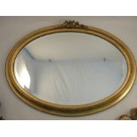 An oval mirror, with a stepped gilt frame and foliate frieze over, mirror plate width 28ins