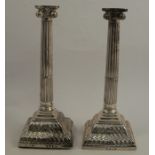 A pair of silver Ionic capital candlesticks, with fluted columns, raised on embossed stepped