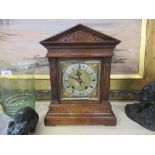 An Edwardian oak mantle clock of architectural form, having a square brass dial flanked by a column,