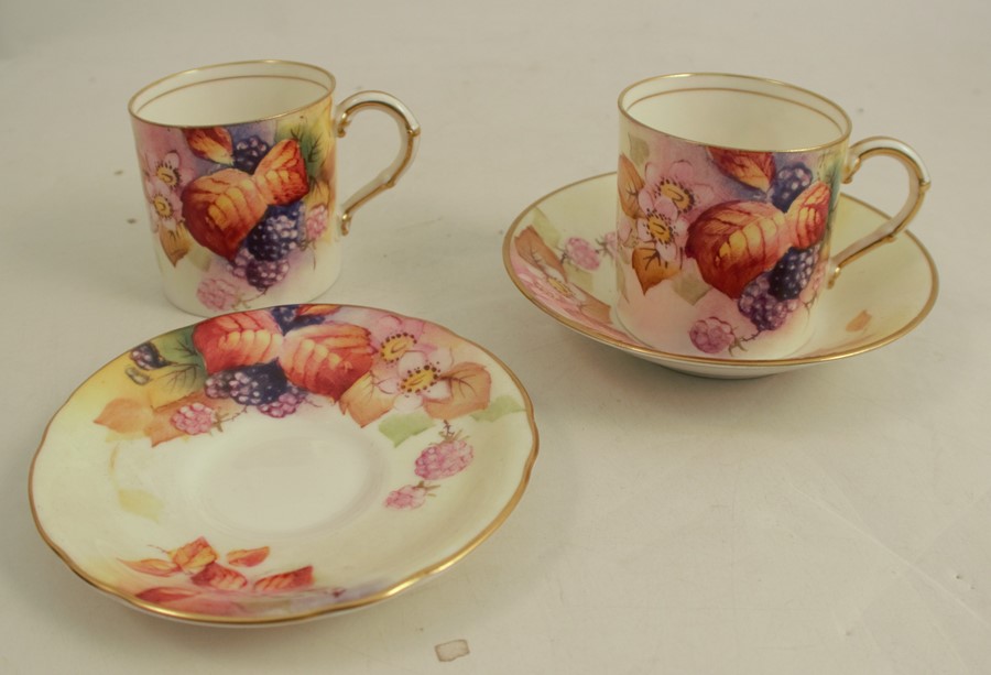 Two Royal Worcester coffee cans and two saucers, decorated with Autumnal fruits and leaves by M