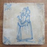 A Delft style pottery tile, decorated with a woman in period dress, 5ins x 5ins
