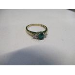 A 9 carat gold emerald and diamond ring, the step cut stone 4.8mm by 3.5mm, flanked either side by a