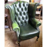 A modern green leatherette wing armchair, with button back, raised on cabriole legs, with fire