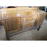 A oak sideboard, with carved decoration to the drawers which are flanked by cupboards, raised on