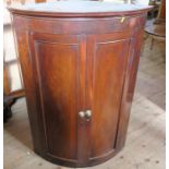A 19th century mahogany barrel front corner cupboard, the two doors opening to reveal shelves,