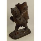 A 19th century black Forest carved wooden figure of a standing bear, carrying a log, with glass