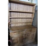 A pine dresser, with close boarded shelves to the back, the base fitted two drawers over two