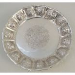 An unmarked silver shaped circular dish, embossed with panels of fruit, engraved to the centre,