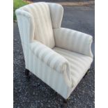 An Edwardian upholstered wing armchair, raised on short cabriole style front legs