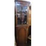 An oak floor standing corner cupboard, the upper section with glazed door, the lower with arched