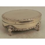 An oval silver dressing table box, with embossed edge, the base being tortoiseshell and raised on