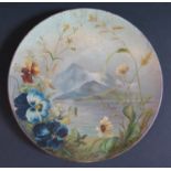 A Watcombe Pottery Terracotta Plate decorated with a landscape and flowers, signed C.R. Brown