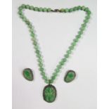 A Carved Jadeite Pendant in a silver filigree setting (43x33mm) on a 52 bead (10mm) necklace (