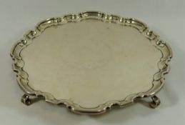 A George IV circular silver tray, Sheffield 1931, with shaped rim, raised on four scroll feet,