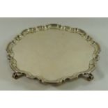 A George IV circular silver tray, Sheffield 1931, with shaped rim, raised on four scroll feet,